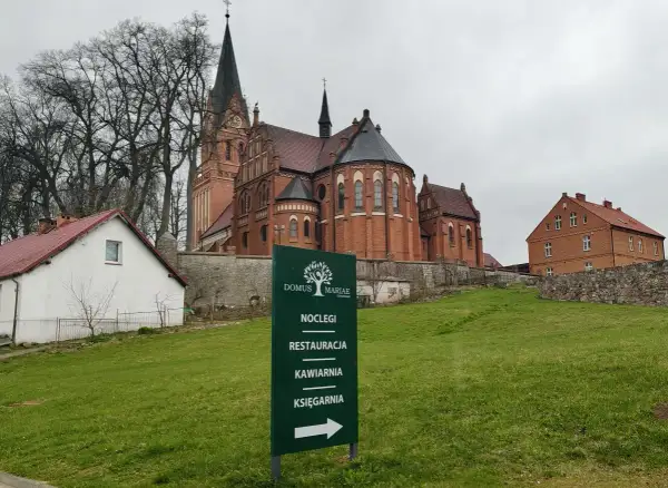 Dom Pielgrzyma w Gietrzwałdzie oferuje noclegi, restaurację, kawiarnię i księgarnię. W tle kościół.