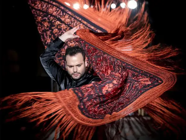 Un bailarín flamenco agita un mantón de Manila de origen oriental, con flecos anaranjados y estampado floral.