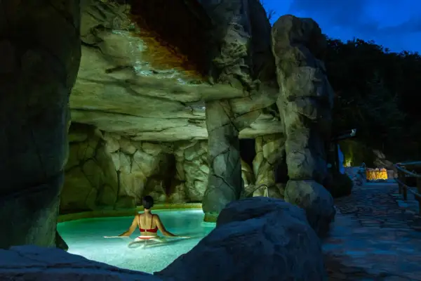 Una mujer disfruta de un relajante spa de noche en una piscina natural rodeada de rocas.