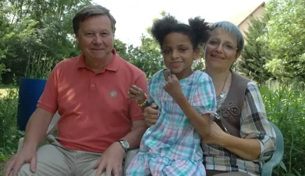 Un homme, une femme et une petite fille souriants, peut-être la famille de Leonard Berducat, profitent d'un moment ensoleillé dans un jardin.