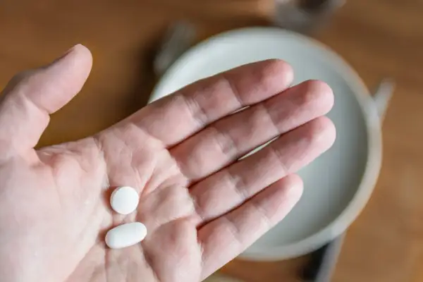 Dłoń trzymająca dwie białe tabletki: okrągłą i owalną.