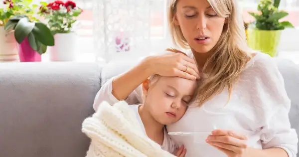 Zmartwiona mama sprawdza temperaturę chorej córki, która śpi otulona kocykiem. Myśli o podaniu Fervex dla dzieci.