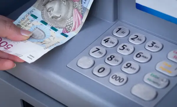 Dłoń wkłada banknot 500 zł do bankomatu. Zastanawiasz się, mbank ile idzie przelew?