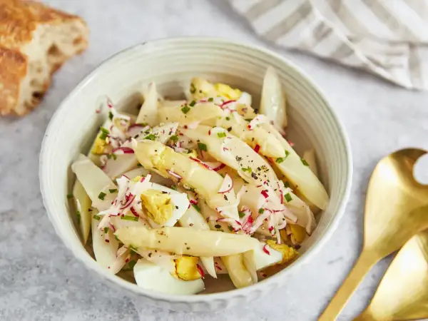 Schüssel mit Spargelsalat mit Ei, Radieschen und Schnittlauch, dazu ein Stück Baguette.