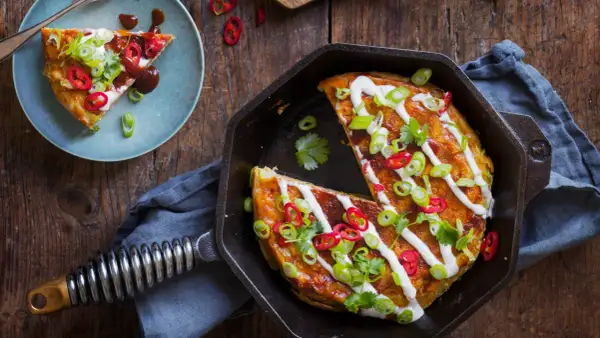 En saftig okonomiyaki i gjutjärnspanna, toppad med gräddfil, salladslök och chili. Ett perfekt recept för en smakrik middag.