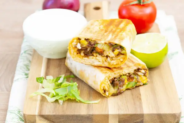 Pyszny burrito przepis: dwa połówki burrito z ryżem, mięsem mielonym, kukurydzą i warzywami, podane z limonką i śmietaną.