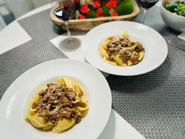 Deux assiettes de pâtes conchiglioni garnies d'une généreuse sauce bolognaise, prêtes à être dégustées avec un verre de vin rouge.