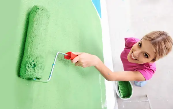 Frauen streichen bei Auszug nach 5 Jahren die Wand grün. Sie lächelt fröhlich, während sie mit der Rolle die Farbe aufträgt.