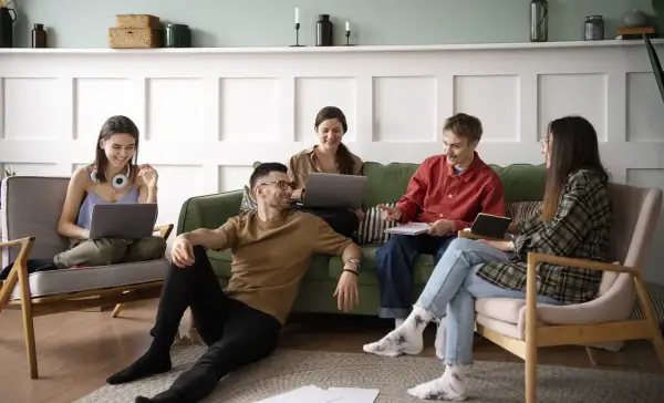 Cinq jeunes discutent et travaillent ensemble dans un salon, une scène typique d'une colocation avec un bail solidaire.