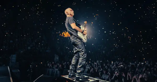 Eros Ramazzotti gra na gitarze podczas koncertu, a tłum w ciemnościach trzyma zapalone telefony.