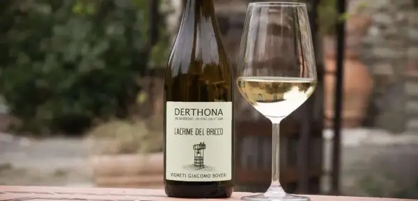 Calice e bottiglia di Derthona, vino Timorasso. Le caratteristiche di questo vino bianco piemontese sono freschezza e note minerali.