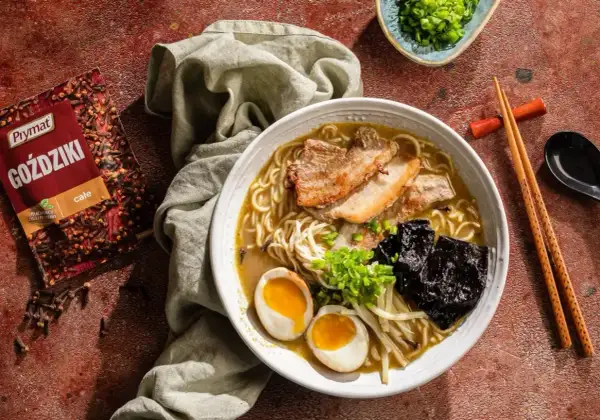 Jak zrobić ramen? Aromatyczny bulion, makaron, jajko na pół, chrupiąca wieprzowina i nori. Obok paczka goździków Prymat.