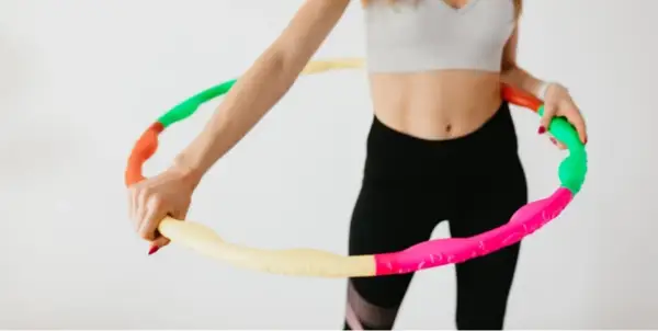 Kobieta w sportowym stroju trzyma kolorową obręcz hula hop. Czy hula hop jest szkodliwe? Nie, to świetna zabawa i trening!