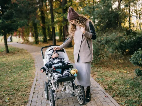 Mama poprawia czapkę malucha, który siedzi w spacerówce. Jesienny spacer po parku.