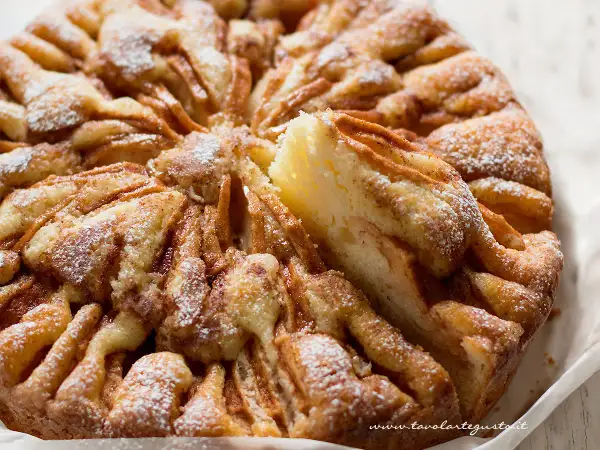 Una deliziosa torta di mele, cosparsa di zucchero a velo, con una fetta sollevata che rivela la morbida consistenza.