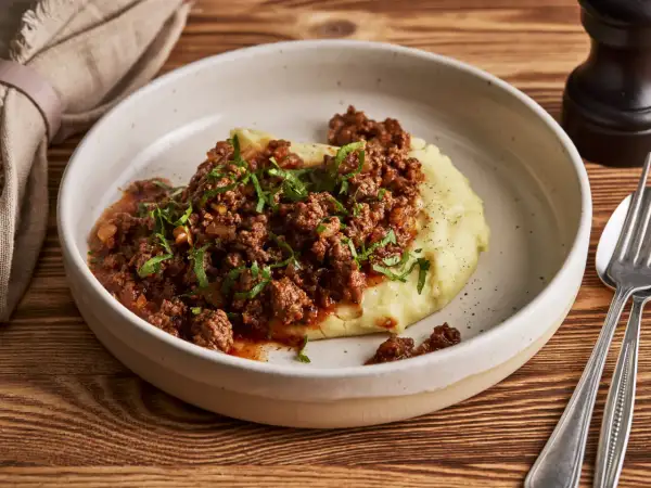 Herzhaftes Hackfleisch mit Tomatensauce auf cremigem Kartoffelpüree, garniert mit Petersilie. Ein einfaches und leckeres Haschee Rezept.
