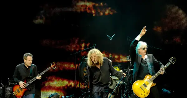 Trzech muzyków na scenie podczas koncertu Led Zeppelin. John Paul Jones gra na basie, Robert Plant śpiewa, a Jimmy Page z uniesioną ręką gra na gitarze.