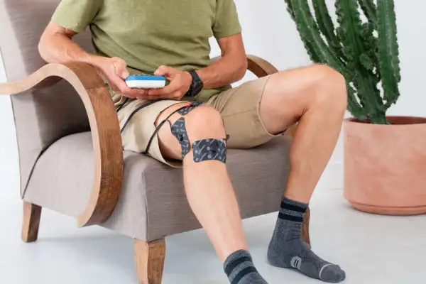Homme assis, utilisant un appareil d'électrostimulation pour le traitement de sa tendinite au genou.