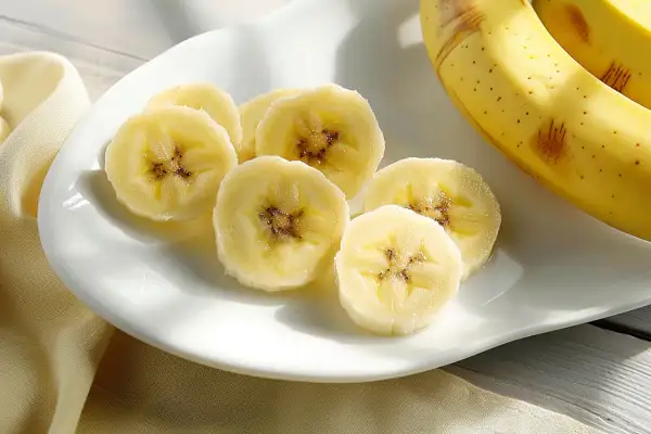 Fette di banana su un piatto bianco, con banane intere sullo sfondo. La banana è astringente o lassativa, a seconda della maturazione.