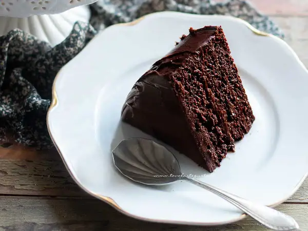 Una fetta di torta al cioccolato, ricca e umida, su un piatto bianco con un cucchiaino d'argento.