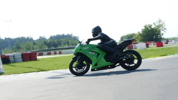 Motocyklista w kombinezonie na zielonym motocyklu ściga się na torze wyścigowym.