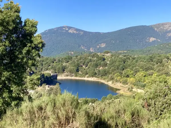 El embalse de Navalmedio, rodeado de bosques y montañas, refleja el cielo azul.