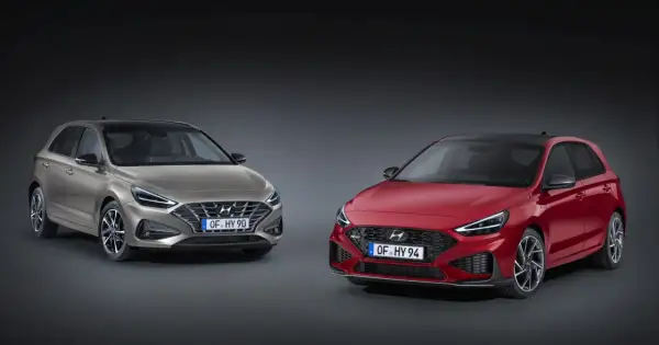 Dwa modele Hyundai i30 2024: jeden w kolorze złotym, drugi w czerwonym, prezentują nowoczesny design i sportowe linie.