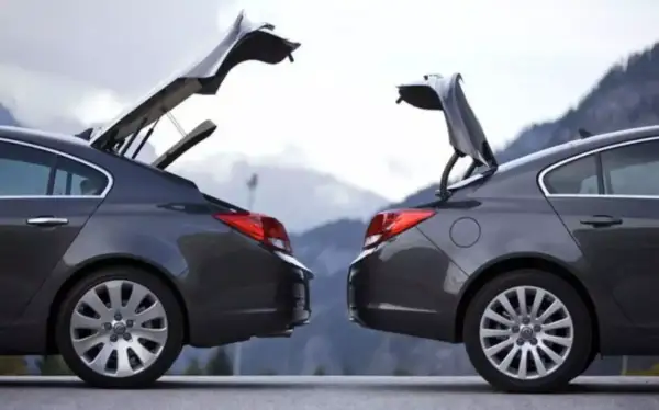 Dwa ciemnoszare sedany z otwartymi bagażnikami, przypominające kształtem hatchback. Góry w tle.