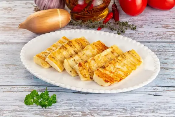 Grillowany ser halloumi na talerzu, idealny do prostych przepisów. W tle czosnek, cebula i pomidory.