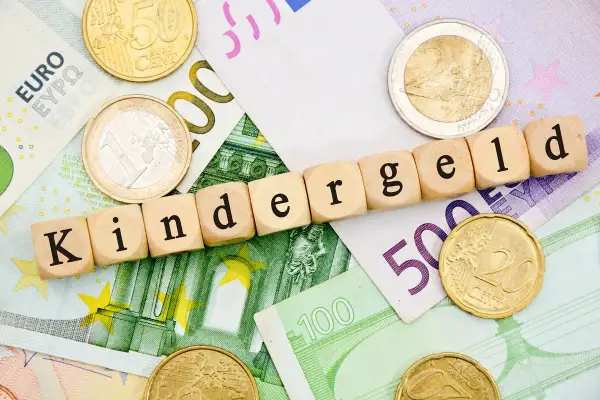 Drewniane klocki z napisem "Kindergeld" leżą na banknotach euro i monetach. Czekamy na Kindergeld 2026!