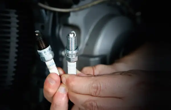 Manos sostienen bujías de moto, una nueva y otra sucia. Saber cada cuanto cambiar bujias moto es clave para el rendimiento.