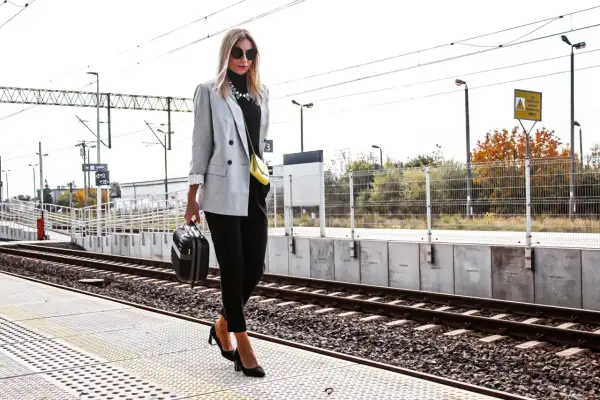 Elegancka szara marynarka damska w stylizacjach na podróż. Kobieta z małą walizką na peronie kolejowym.