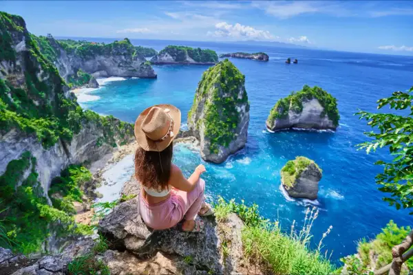 Vue imprenable sur la côte de Bali. Une femme assise au bord d'une falaise admire les îlots verdoyants et l'océan bleu. Idéal pour savoir que faire à Bali.