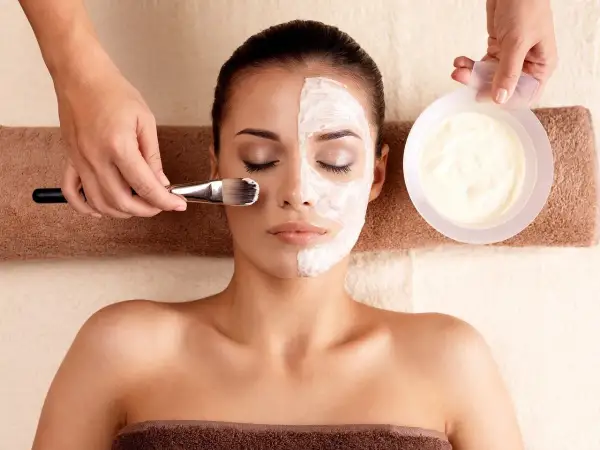 Una mujer recibe un tratamiento facial con una mascarilla aplicada con brocha.