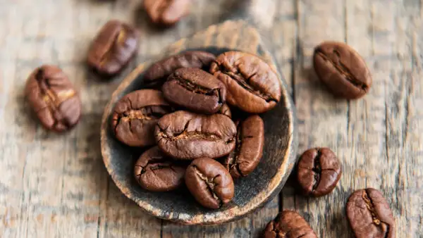 Chicchi di caffè tostati su un cucchiaio di legno, simbolo di alta qualità di caffè.