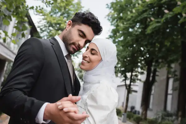 Un uomo in abito scuro e una donna con velo bianco si abbracciano teneramente, celebrando il loro matrimonio misto.