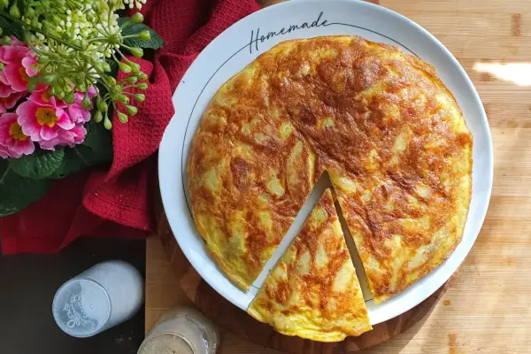 A golden-brown potato frittata with a slice cut out, on a white plate with "Homemade" written on it.