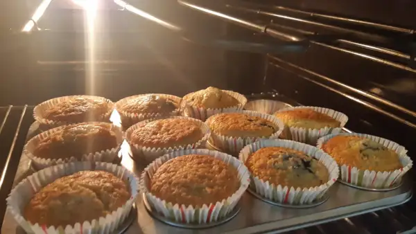 En plåt med nybakade glutenfria muffins i ugnen. Ljuset från ugnen lyser upp de gyllene muffinsarna.