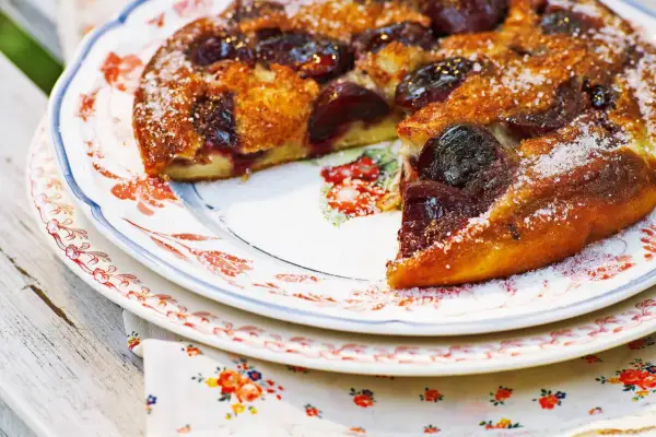 Ein goldbrauner Pfannkuchen mit Kirschen, bestreut mit Zucker, auf einem Teller mit Blumenmuster.