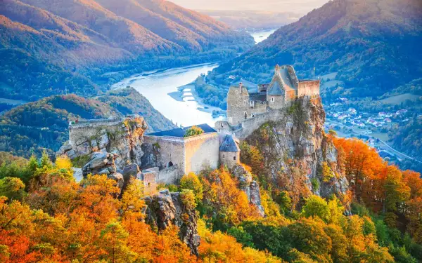 Zamek na skale w dolinie Wachau, otoczony jesiennymi barwami, z rzeką w tle.