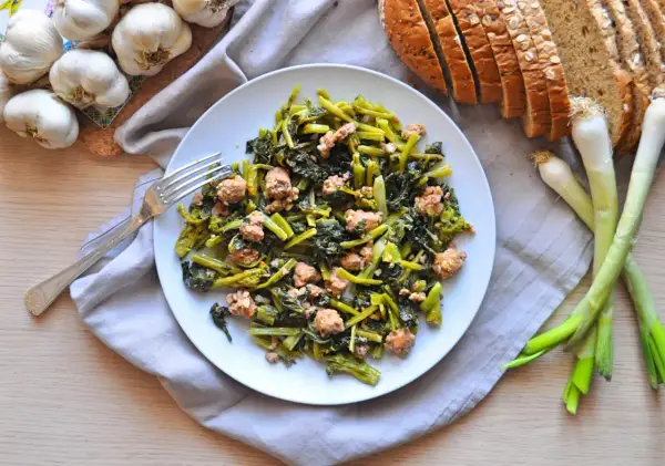 Un piatto di salsiccia e rape saltate, con pane integrale, aglio e cipollotti freschi.