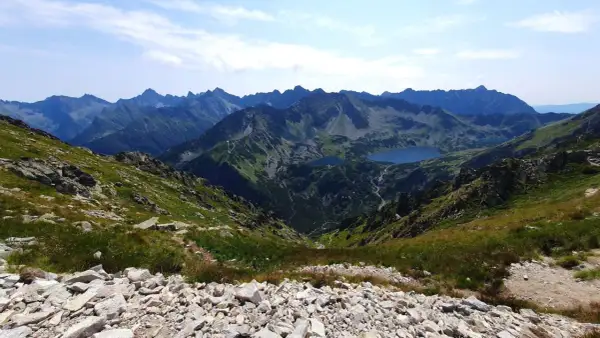 Widok z przełęczy na skraju Orlej Perci na Tatry Wysokie. Dwa jeziora w dolinie, skaliste zbocza i szczyty w oddali.