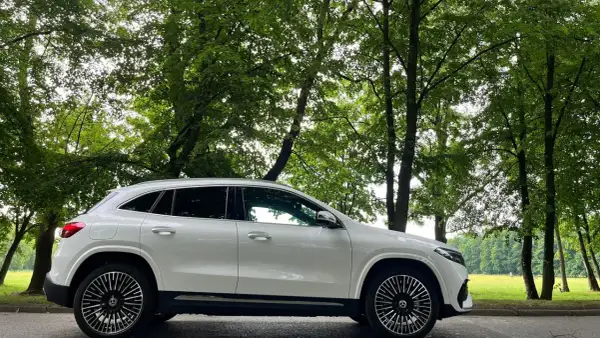 Biały Mercedes EQA stoi na tle zielonego, leśnego krajobrazu.