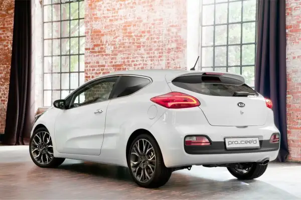 Biały Kia Pro_Ceed 1.6 benzyna z eleganckimi felgami stoi w stylowym wnętrzu z ceglaną ścianą i dużymi oknami.