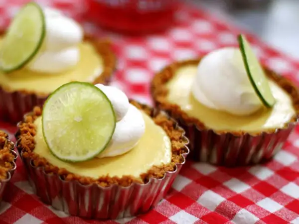 Små key lime pies med vispad grädde och limeklyfta på en rödvitrutig duk.