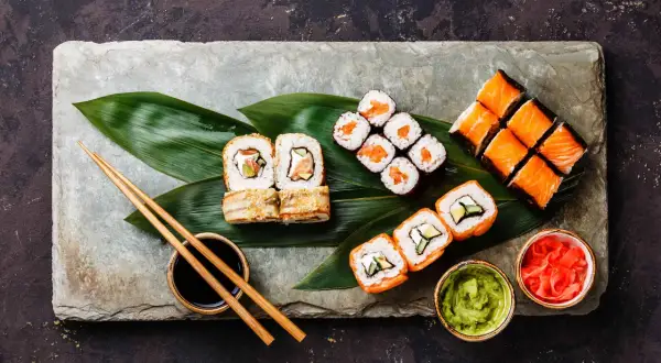 Sushi-Platte mit Lachs-Rollen, Nigiri und Beilagen. So isst man Sushi richtig: mit Stäbchen, Sojasauce, Wasabi und eingelegtem Ingwer.