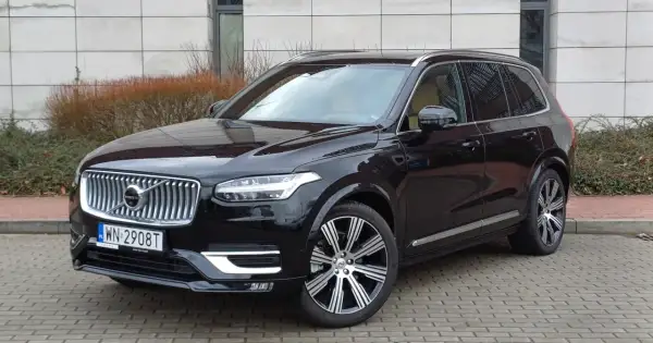 Elegancki, czarny Volvo XC90 z chromowanymi felgami stoi na brukowanym podjeździe.