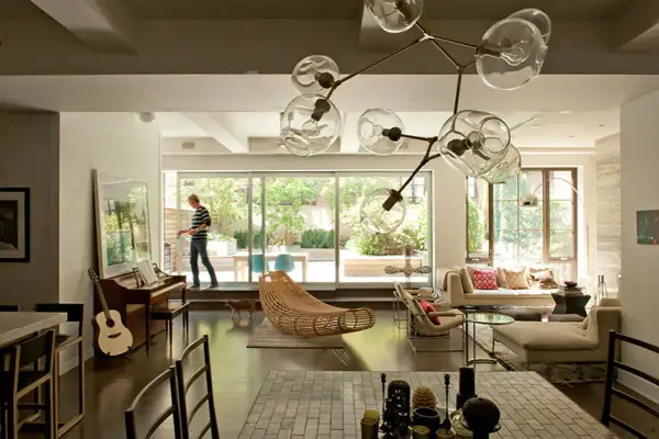 A man walks through a modern living room, captured in this interior architecture photography. A piano, guitar, and unique light fixture are visible.