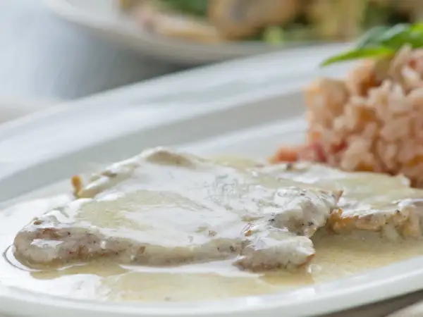 Zartes Putenschnitzel mit cremiger Rahmsauce, serviert mit einer Beilage aus Reis. Ein köstliches Gericht.