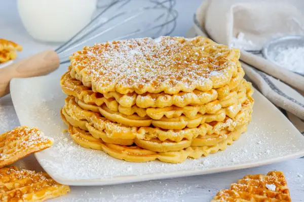 Stapel goldbrauner Waffeln ohne Backpulver, bestäubt mit Puderzucker. Daneben liegen weitere Waffeln.